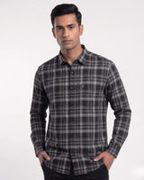 A man wearing a long-sleeve black and gray plaid button-down shirt, standing against a plain light gray background.