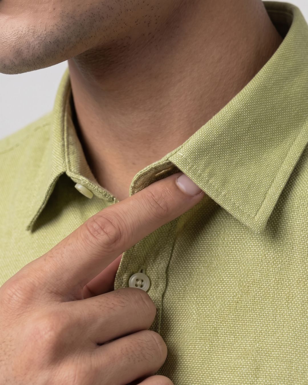 Close-up of a person wearing a light olive green textured polo shirt, pointing to the collar and button area with their finger.