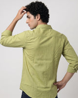 A man wearing a light olive green long-sleeve linen shirt, shown from the back against a plain light gray studio background.