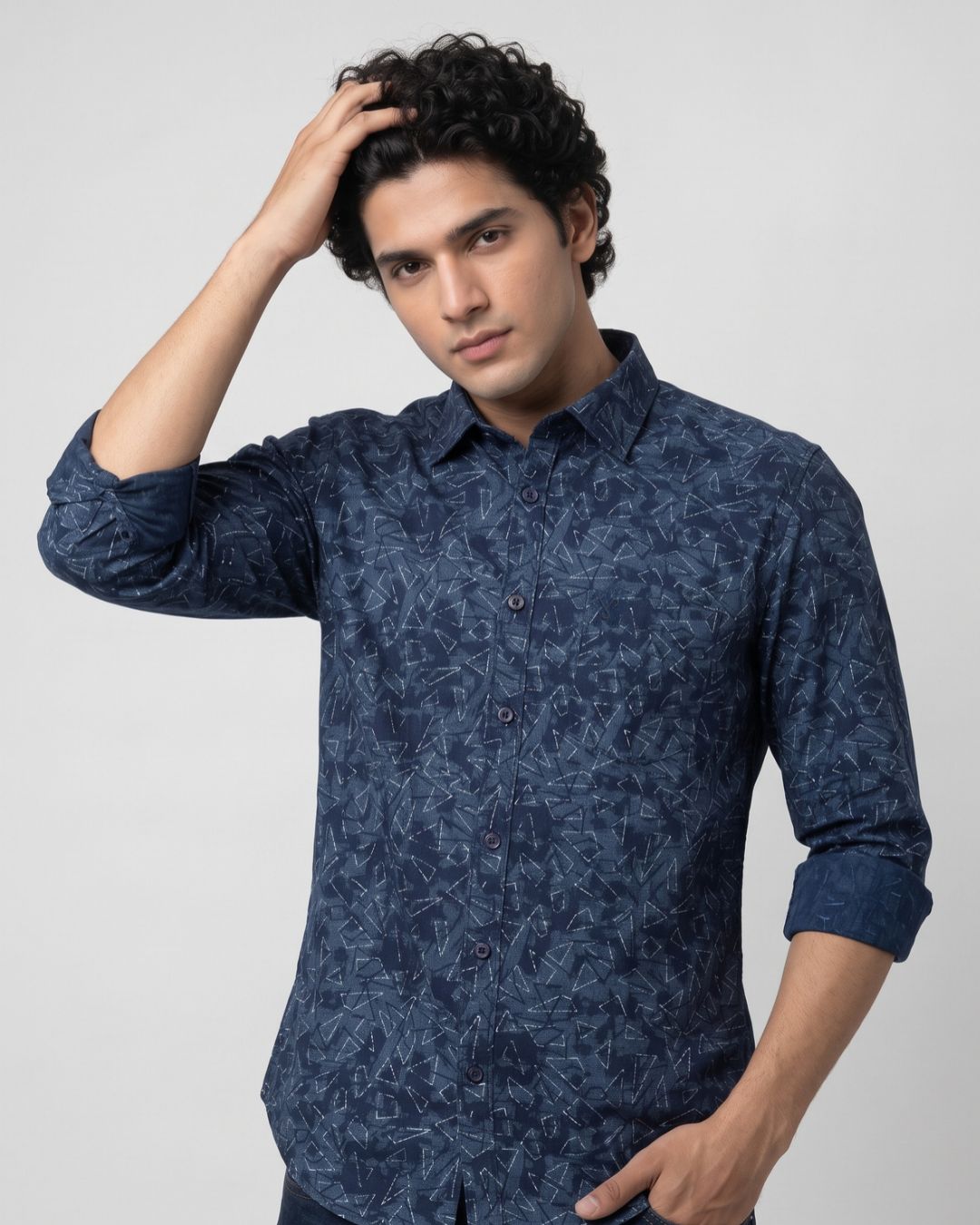 A man wearing a dark blue patterned long-sleeve button-up shirt, posing against a light gray studio background.