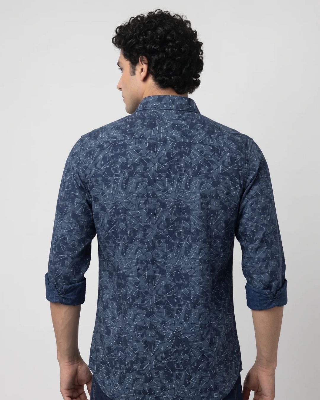 A man wearing a dark blue patterned long-sleeve button-up shirt, posing against a light gray studio background.
