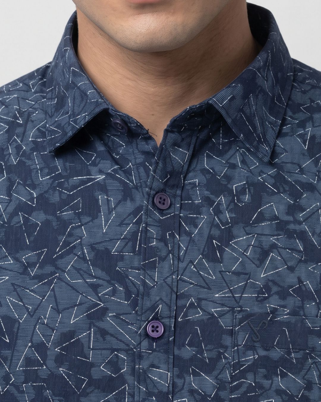 A man wearing a dark blue patterned long-sleeve button-up shirt, posing against a light gray studio background.