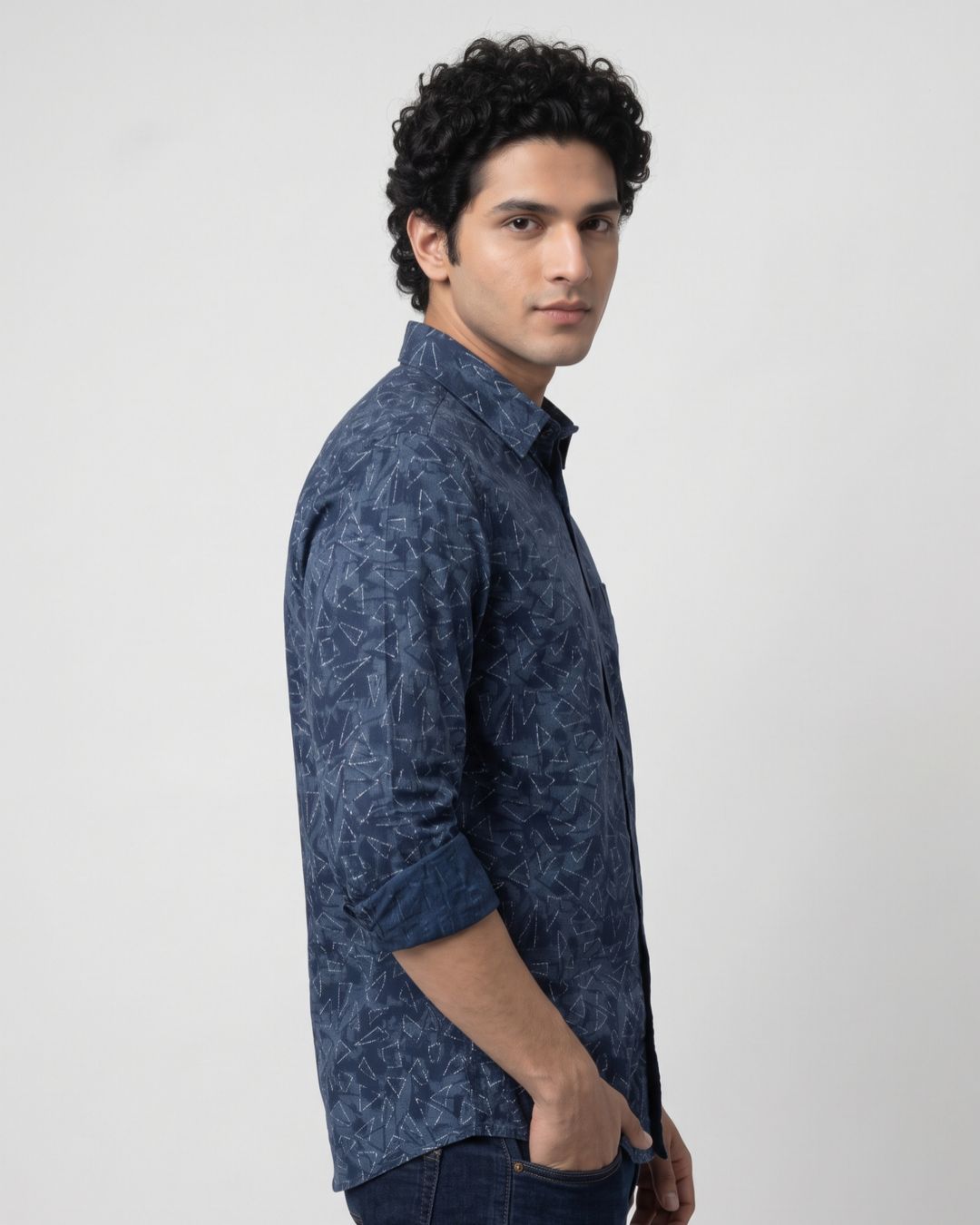 A man wearing a dark blue patterned long-sleeve button-up shirt, shown in a side profile against a plain light gray background.