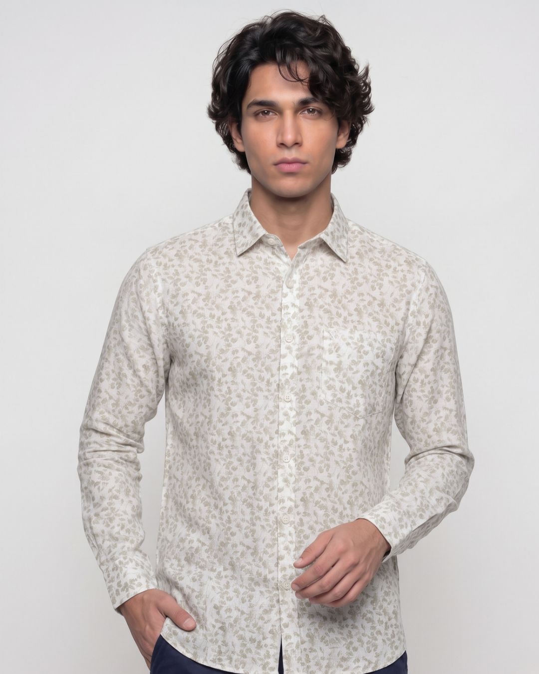 A man wearing a long-sleeve button-up shirt with a light beige and white floral pattern, posed against a solid light gray background.