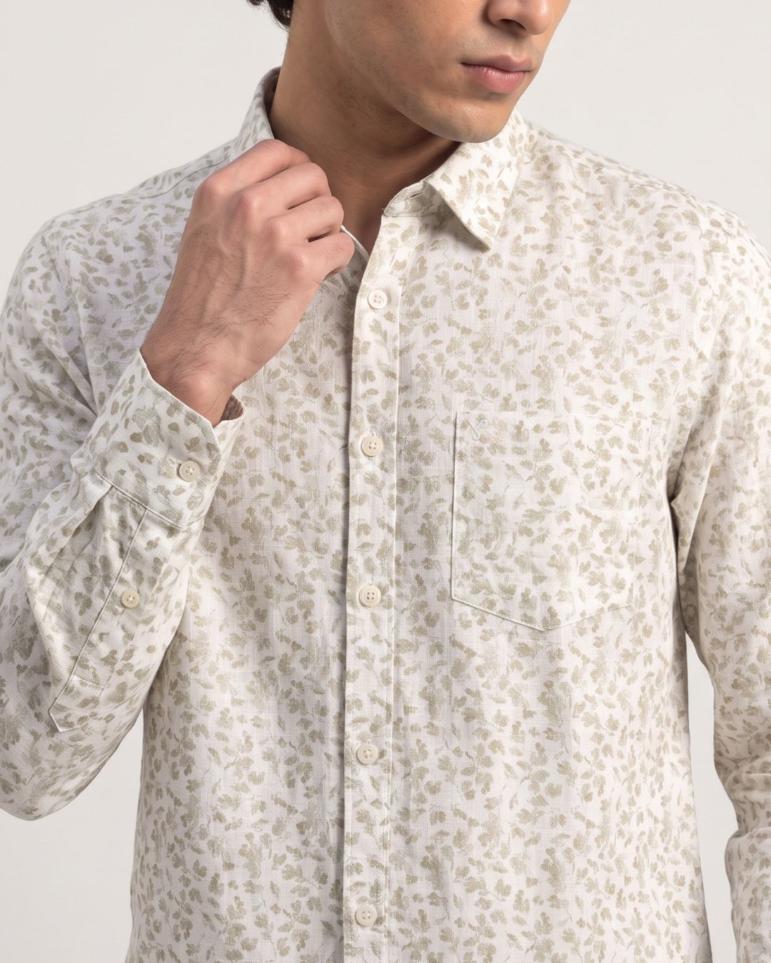 A close-up of a man wearing a long-sleeve button-up shirt with a beige and off-white animal print pattern, adjusting the collar.