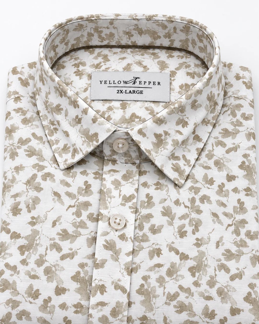A folded men's button-down shirt by Yellow Pepper, featuring a delicate beige and brown floral pattern on a white background. The collar label clearly reads 'YELLOW PEPPER IN LARGE'.