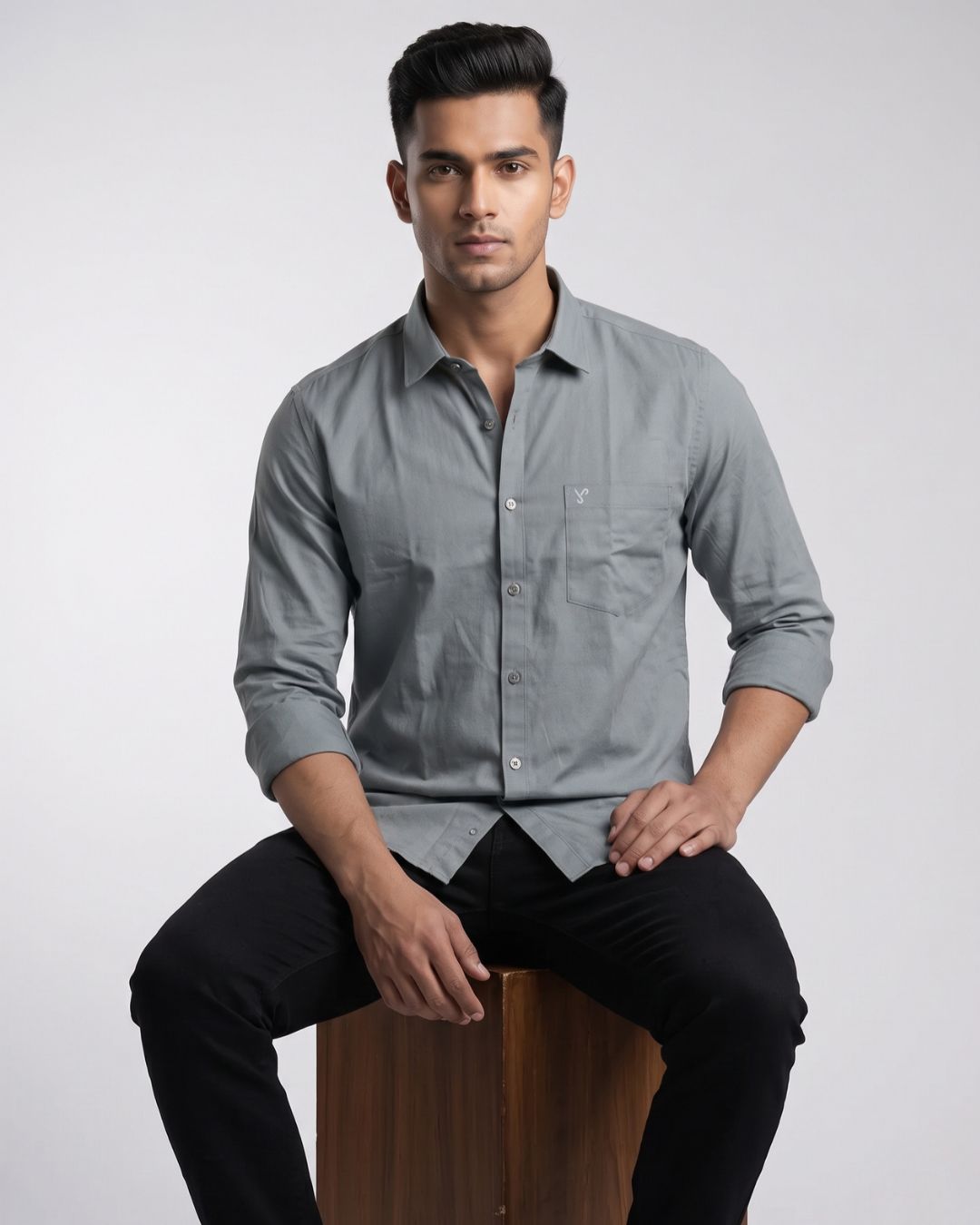 A man wearing a light gray long-sleeve button-down shirt with a chest pocket, posed against a neutral light gray studio background.