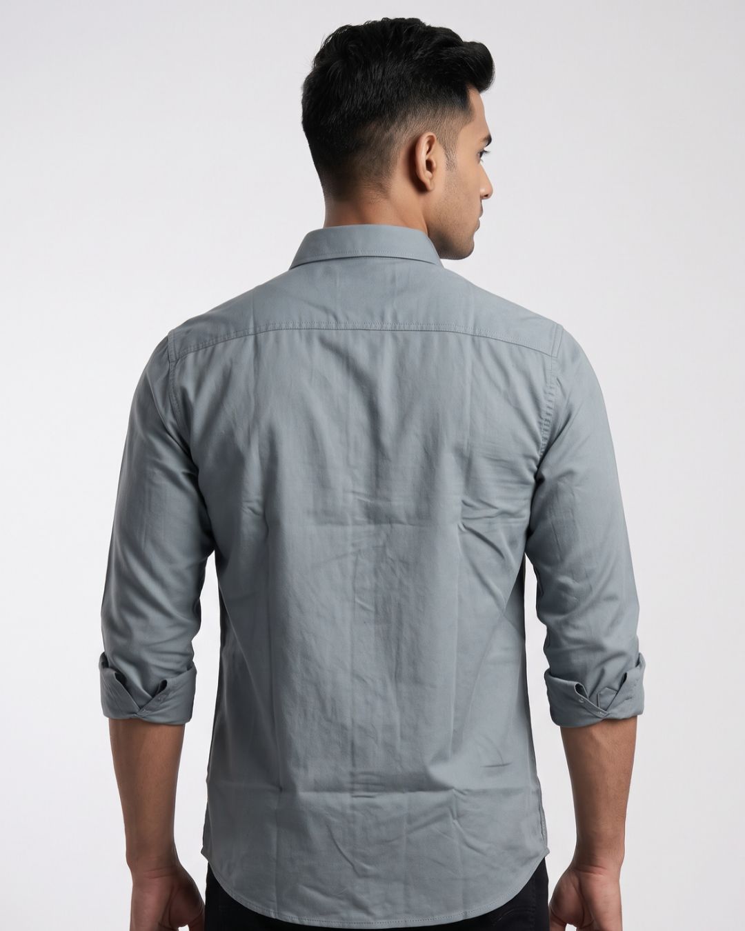 A man wearing a light gray long-sleeve button-down shirt with a chest pocket, posed against a neutral light gray studio background.