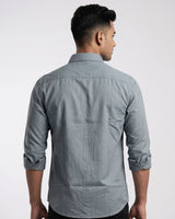 A man wearing a light gray long-sleeve button-down shirt with a chest pocket, posed against a neutral light gray studio background.