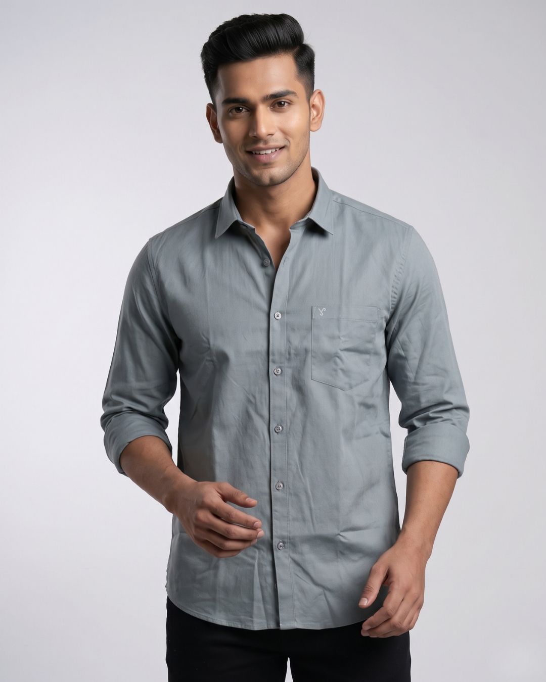 A man wearing a light gray long-sleeve button-down shirt with a chest pocket, posed against a neutral light gray studio background.