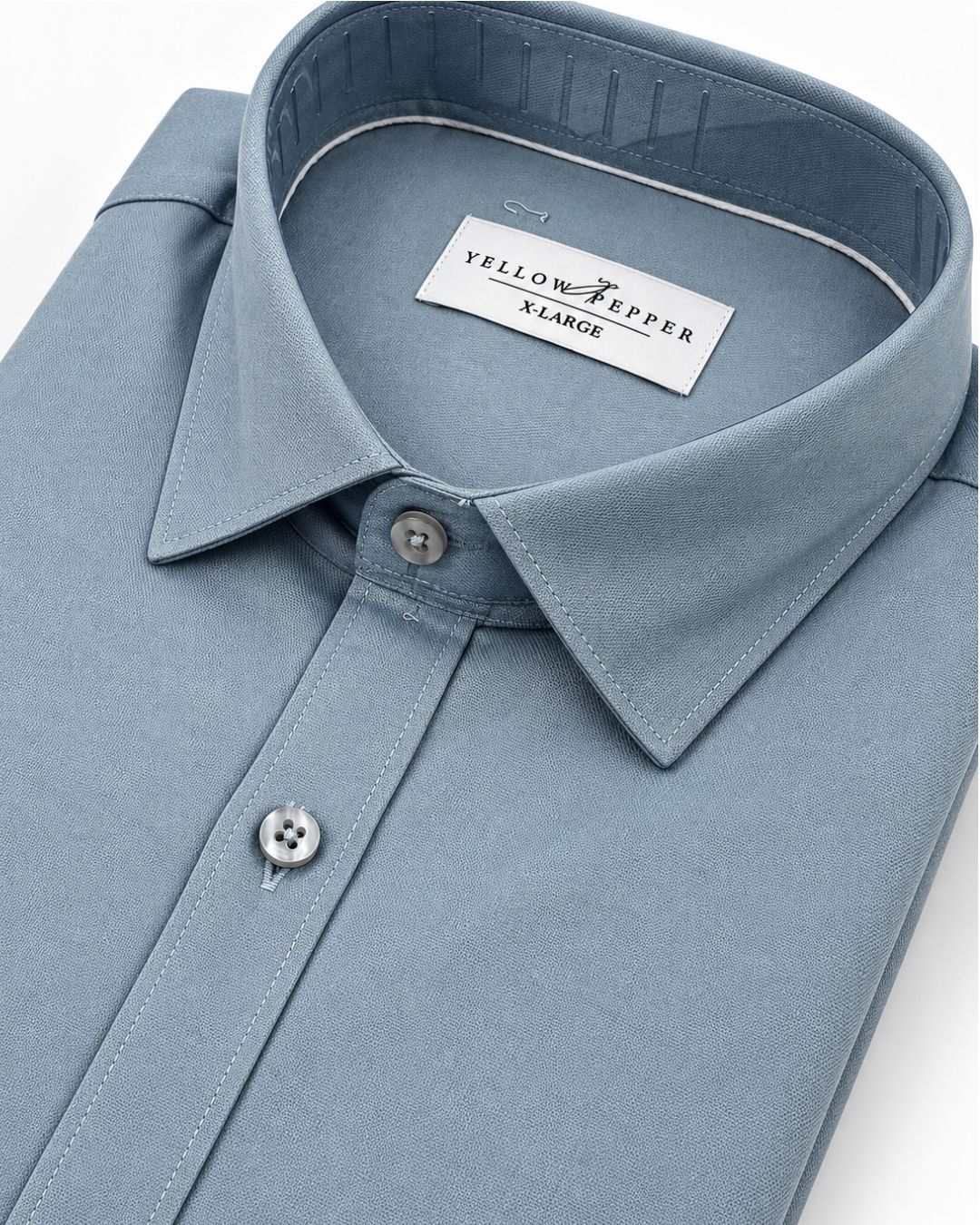 A folded light blue dress shirt with a pointed collar and silver buttons, showing the Yellow & Pepper X-Large brand label inside the collar, shot on a clean white background.