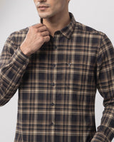 A man wearing a long-sleeve button-down plaid shirt in dark navy and beige, adjusting the collar. The shirt features a small embroidered logo on the left chest pocket.