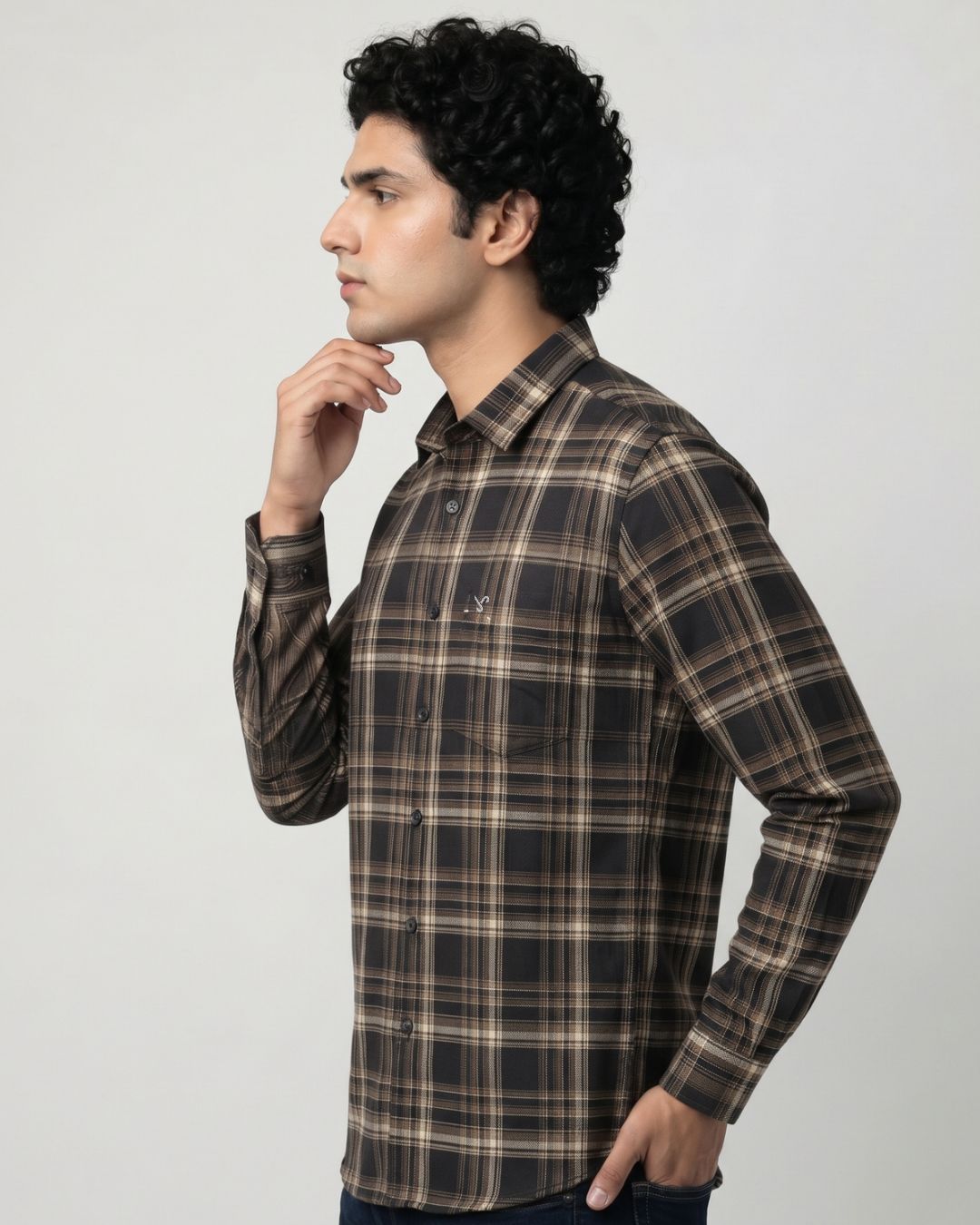 A man wearing a brown and beige plaid long-sleeve button-up shirt, shown in profile against a light gray studio background.