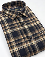 A folded long-sleeve plaid button-up shirt by The Lancer, featuring a navy blue, beige, and brown tartan pattern with a small white embroidered logo on the chest.