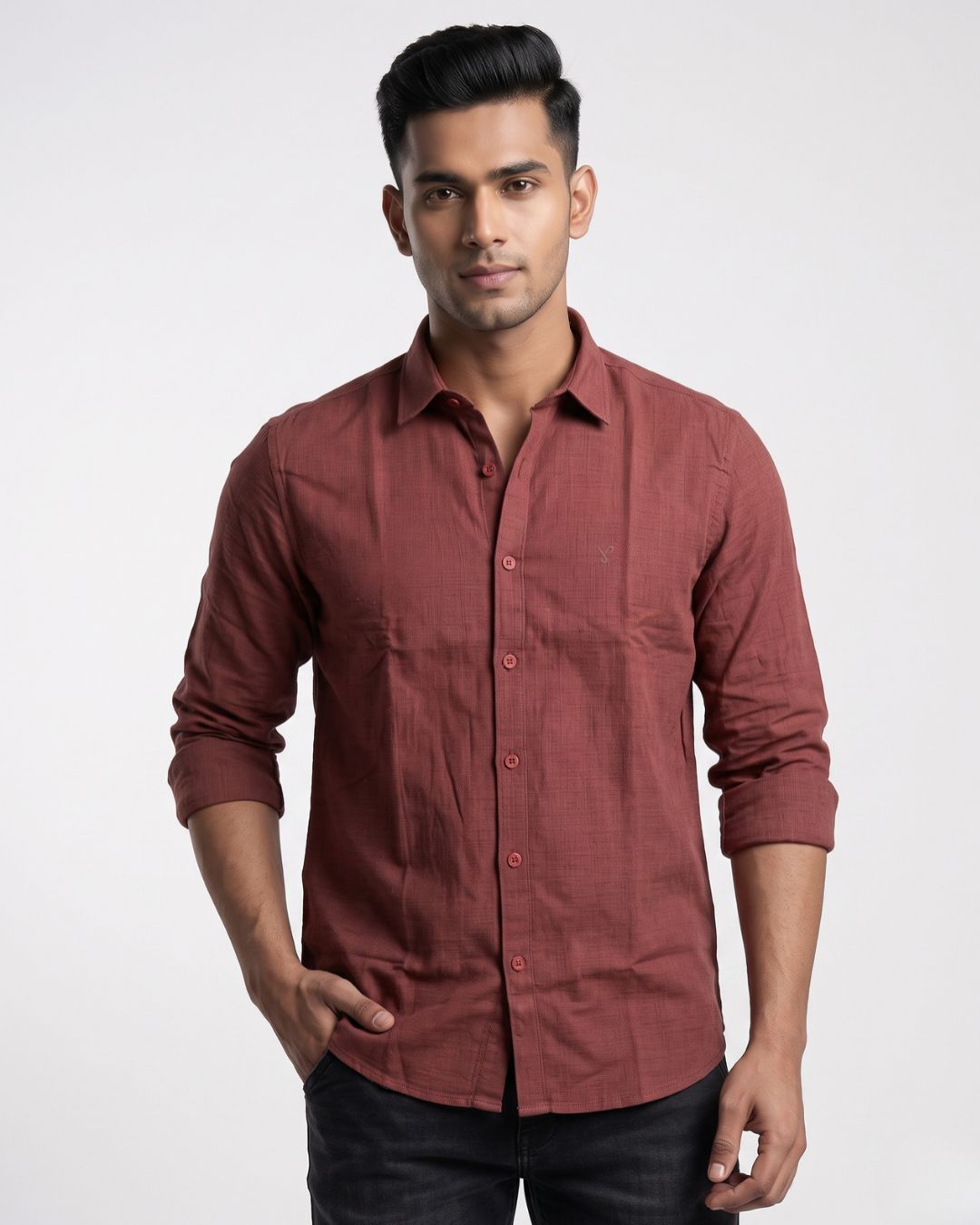 A man wearing a long-sleeve button-up shirt in a dusty rose or muted terracotta color, paired with dark jeans, standing against a light gray studio background.