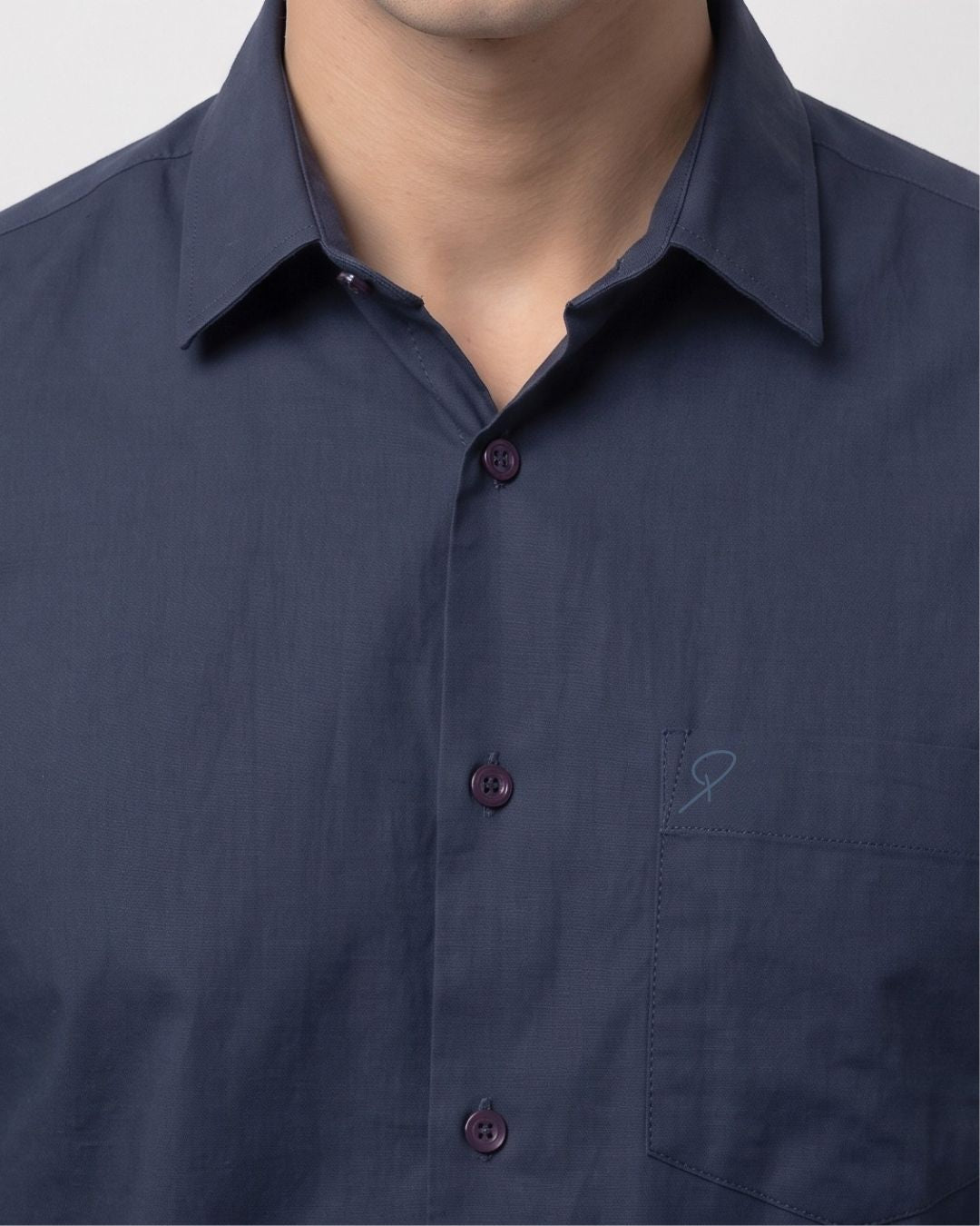 Close-up of a man wearing a dark navy blue button-down shirt with a pointed collar and a small embroidered logo on the chest pocket.