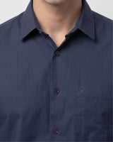 Close-up of a man wearing a dark navy blue button-down shirt with a pointed collar and a small embroidered logo on the chest pocket.