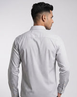 A man shown from the back wearing a light gray and white micro-patterned long-sleeve button-down shirt against a light gray studio background.