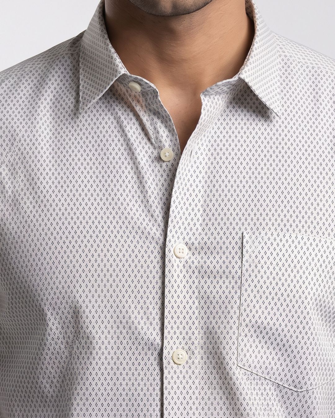 "Man wearing a white printed long-sleeve casual shirt with black trousers while sitting on a wooden chair."
