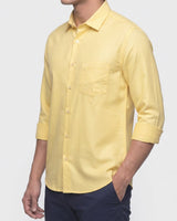 A man wearing a light yellow long-sleeve button-down shirt with a chest pocket, paired with navy blue pants, shown against a plain light gray background.