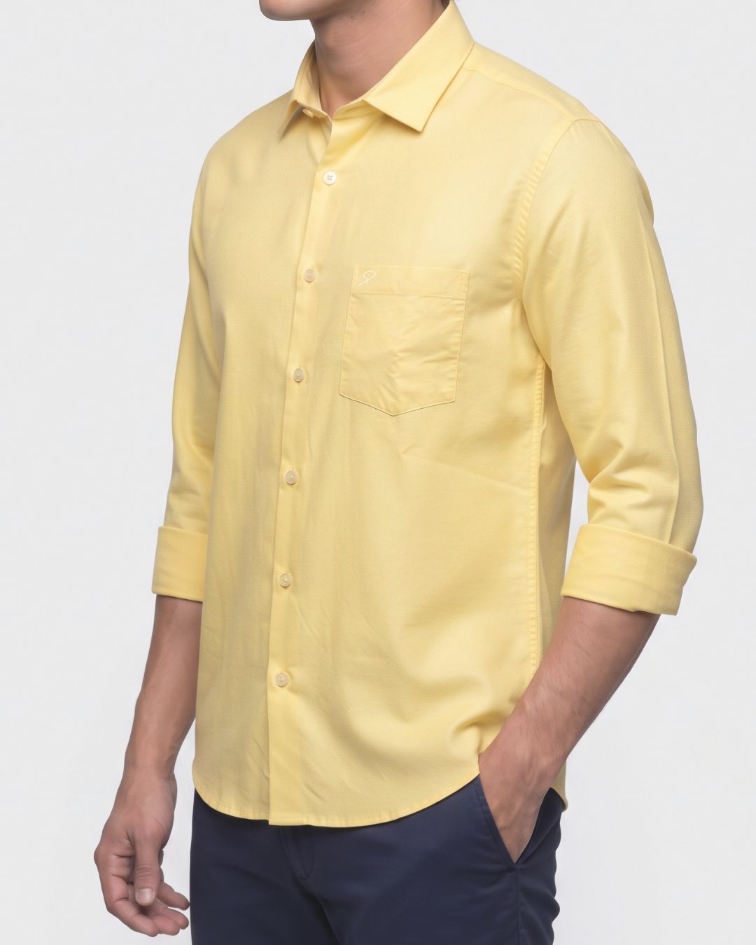 A man wearing a light yellow long-sleeve button-down shirt with a chest pocket, paired with navy blue pants, shown against a plain light gray background.