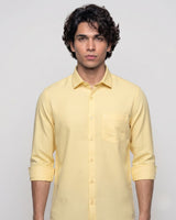 A man wearing a pale yellow long-sleeve button-up shirt with a chest pocket, photographed against a plain light gray studio background.