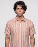 A man wearing a short-sleeve button-up shirt with vertical peach and white stripes, photographed against a light gray studio background.