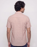 A man viewed from the back wearing a short-sleeve button-up shirt with vertical pink and white stripes, paired with dark navy pants, against a plain light gray background.