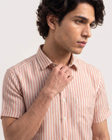 A man wearing a short-sleeve button-up shirt with vertical peach and white stripes, shown from the chest up against a light gray studio background.