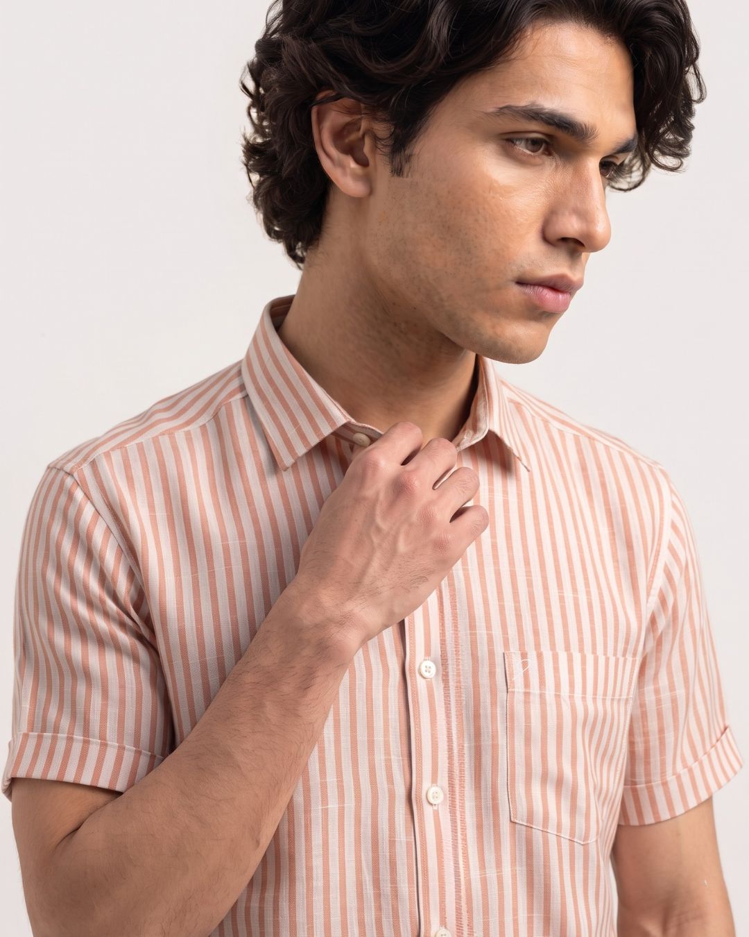 A man wearing a short-sleeve button-up shirt with vertical peach and white stripes, shown from the chest up against a light gray studio background.