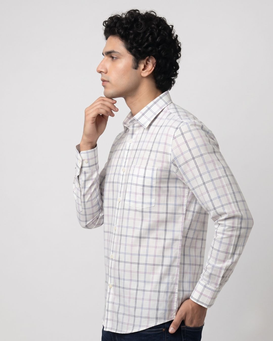 A man wearing a white long-sleeve button-up shirt with a subtle light blue and gray grid pattern, posed in profile against a light gray studio background.