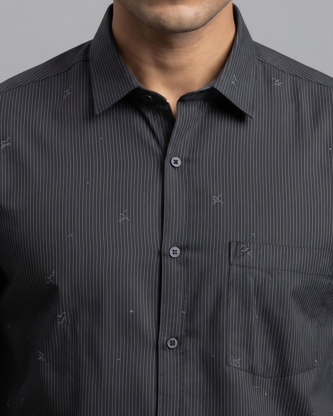 A close-up of a man wearing a dark gray and black pinstriped button-down shirt with a subtle embroidered pattern, showing the collar, chest, and front buttons.