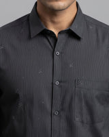A close-up of a man wearing a dark gray and black pinstriped button-down shirt with a subtle embroidered pattern, showing the collar, chest, and front buttons.