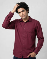 A man wearing a long-sleeve button-down shirt in maroon, posing against a light gray studio background.