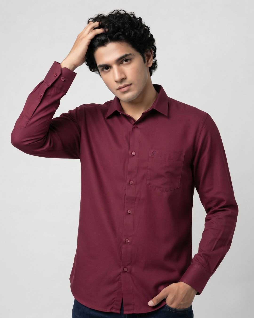 A man wearing a long-sleeve button-down shirt in maroon, posing against a light gray studio background.