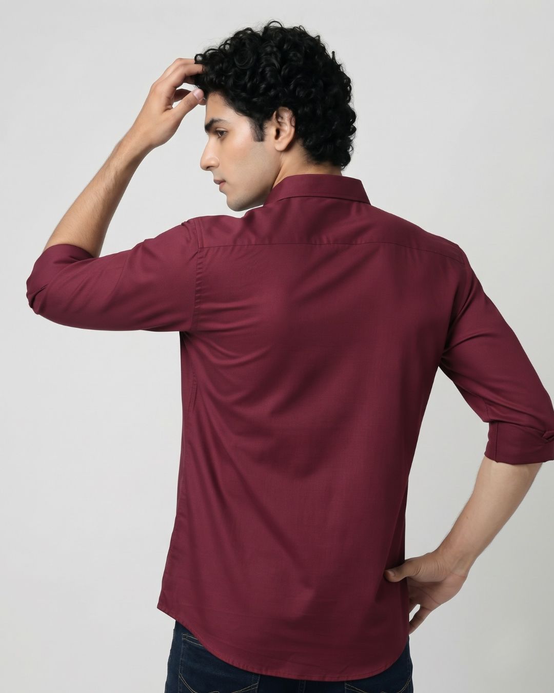 A man wearing a burgundy long-sleeve button-down shirt, shown from the back and side against a plain light gray studio background.