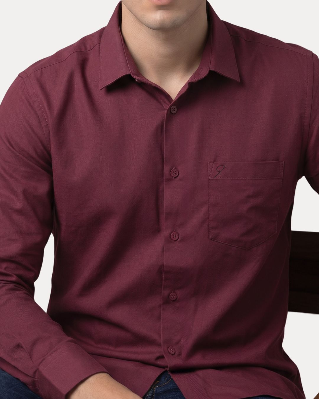 A man wearing a long-sleeve button-down shirt in a deep burgundy or maroon color, shown from the neck down against a light gray background.
