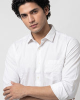 A man wearing a white long-sleeve button-down shirt with a chest pocket, posed against a light gray studio background.