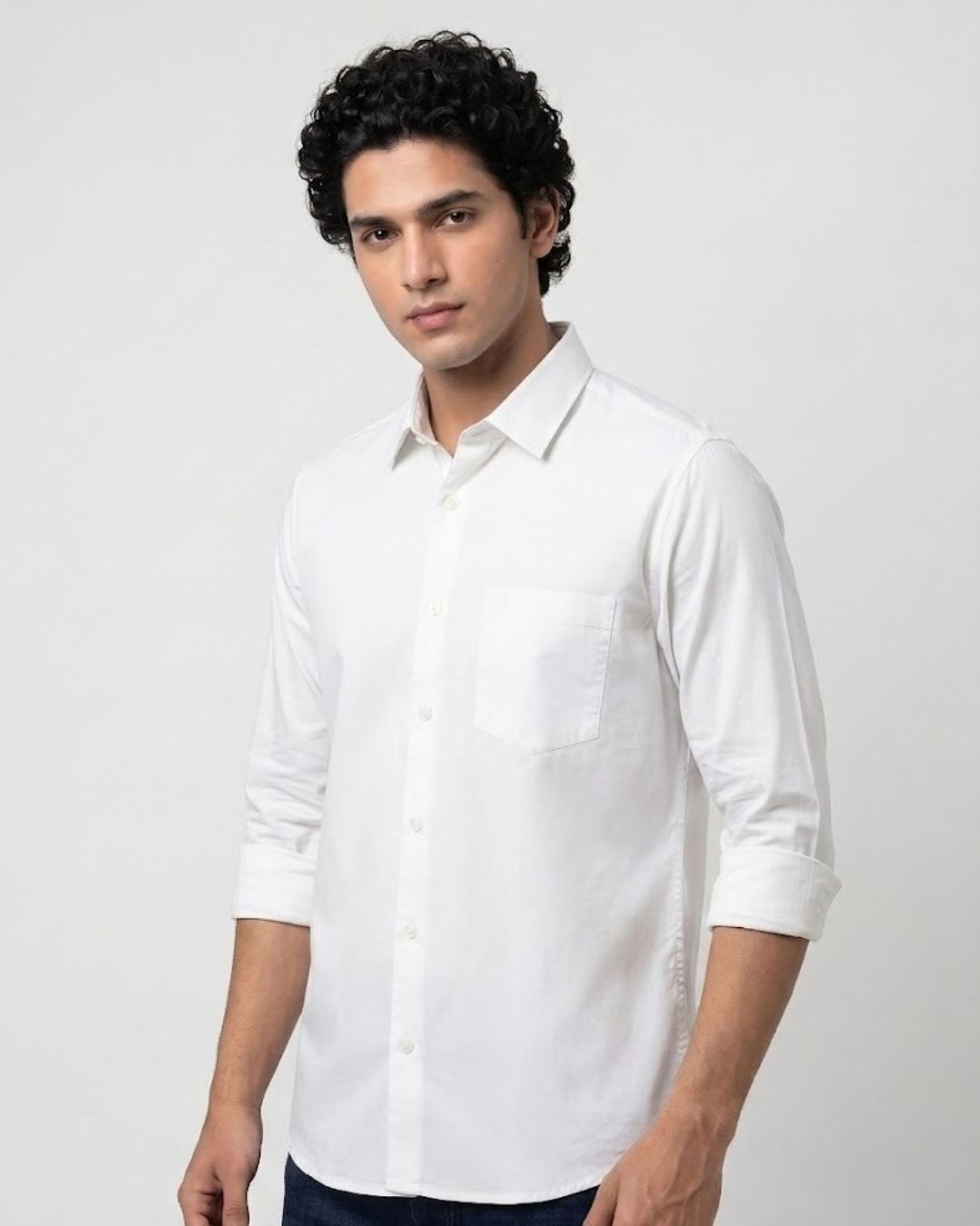 A man wearing a white long-sleeve button-down shirt with a single chest pocket, photographed against a plain light gray studio background.