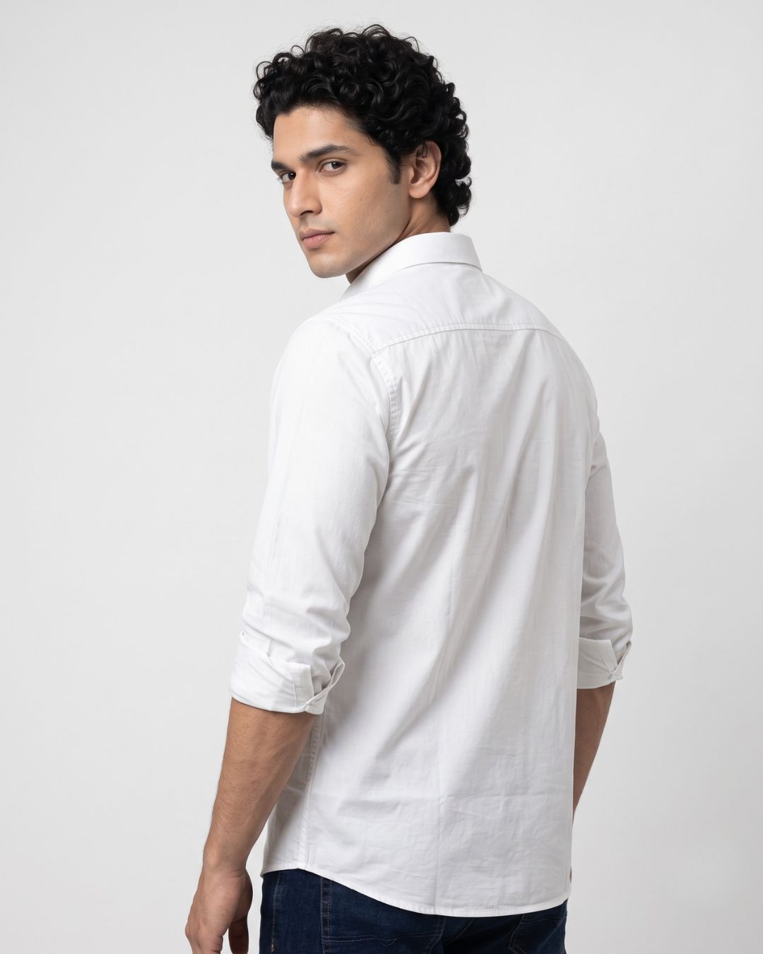 A man wearing a white long-sleeve button-down shirt, shown from a three-quarter back view against a light gray studio background.