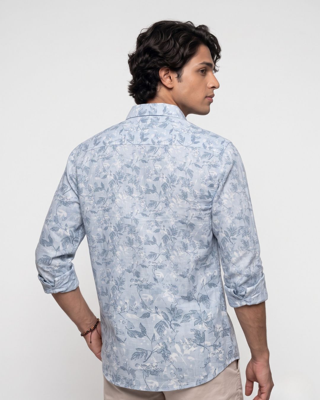A man wearing a light blue and white floral patterned long-sleeve shirt, shown from the back and side against a plain light gray background.