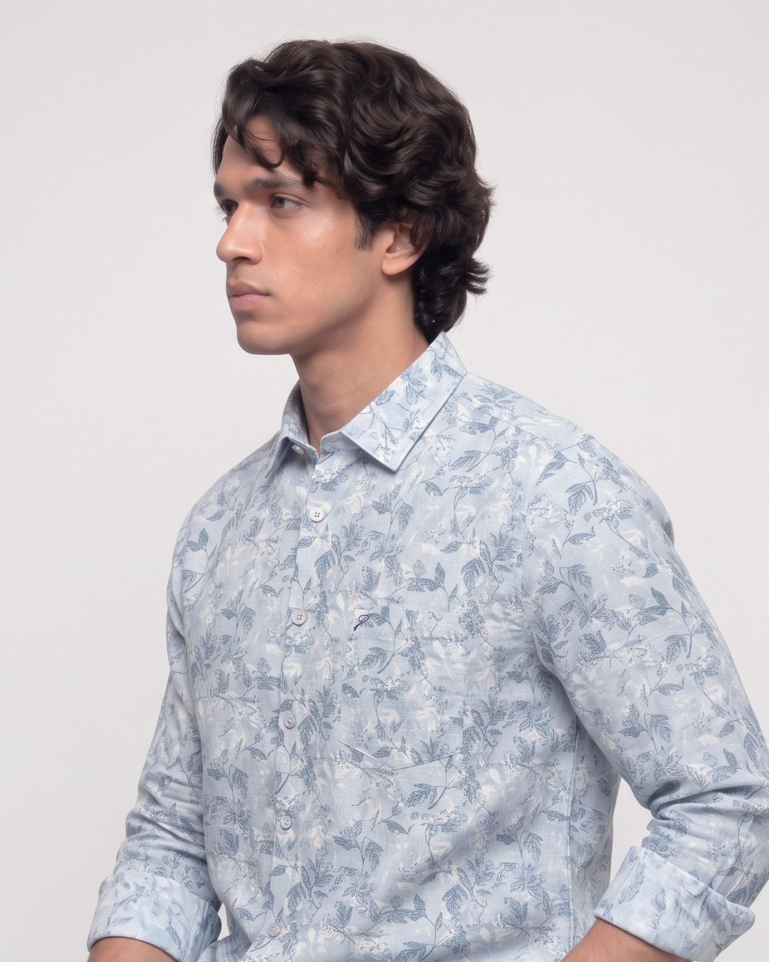 A man wearing a light blue and white floral print long-sleeve button-down shirt, shown in a side profile against a plain light gray background.
