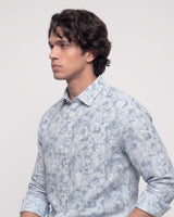 A man wearing a light blue and white floral print long-sleeve button-down shirt, shown in a side profile against a plain light gray background.