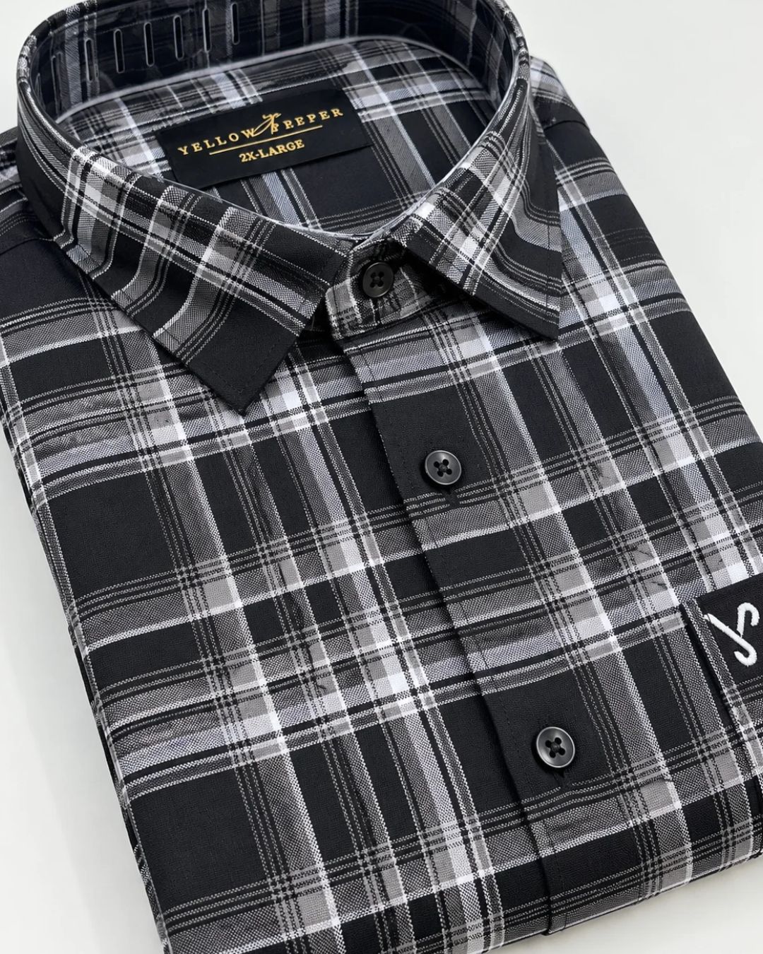 A folded long-sleeve plaid button-up shirt in black, gray, and white, with a visible Yellow River brand label inside the collar.