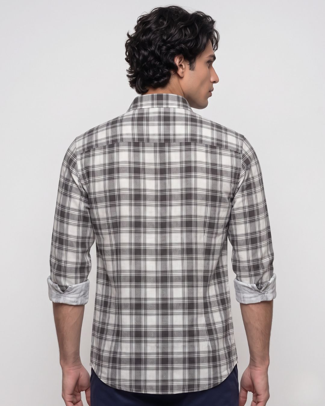 A man wearing a gray and white plaid button-down shirt, photographed from the chest up against a light gray studio background.