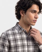 A man wearing a gray, white, and black plaid button-down shirt, shown in a close-up profile view against a light gray background.
