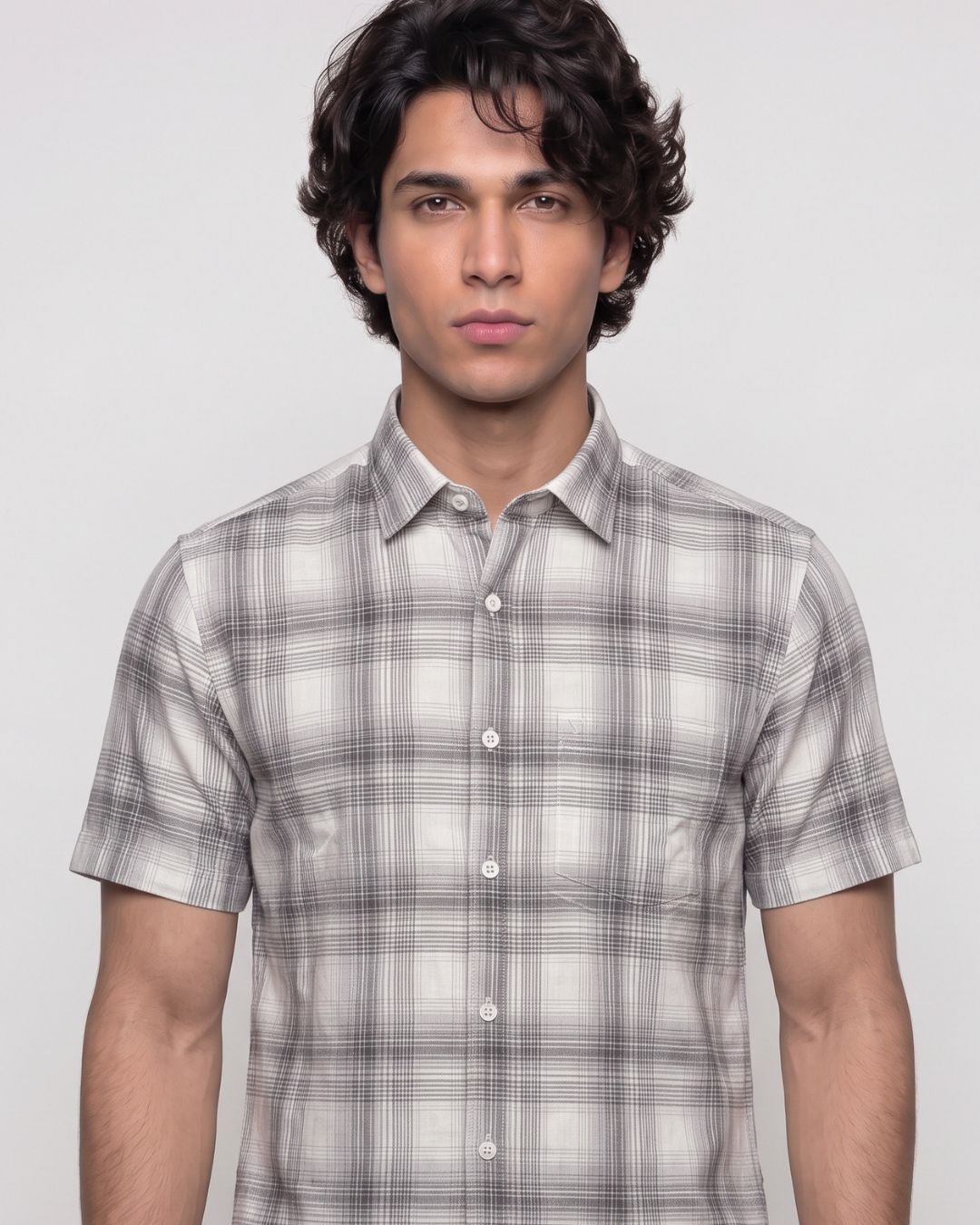 A man wearing a short-sleeve button-up shirt with a gray and white plaid pattern, photographed against a light gray studio background.
