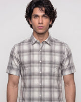 A man wearing a short-sleeve button-up shirt with a gray and white plaid pattern, photographed against a light gray studio background.