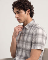 A man wearing a short-sleeve plaid button-up shirt in gray, white, and black, shown in a side profile against a light gray background.