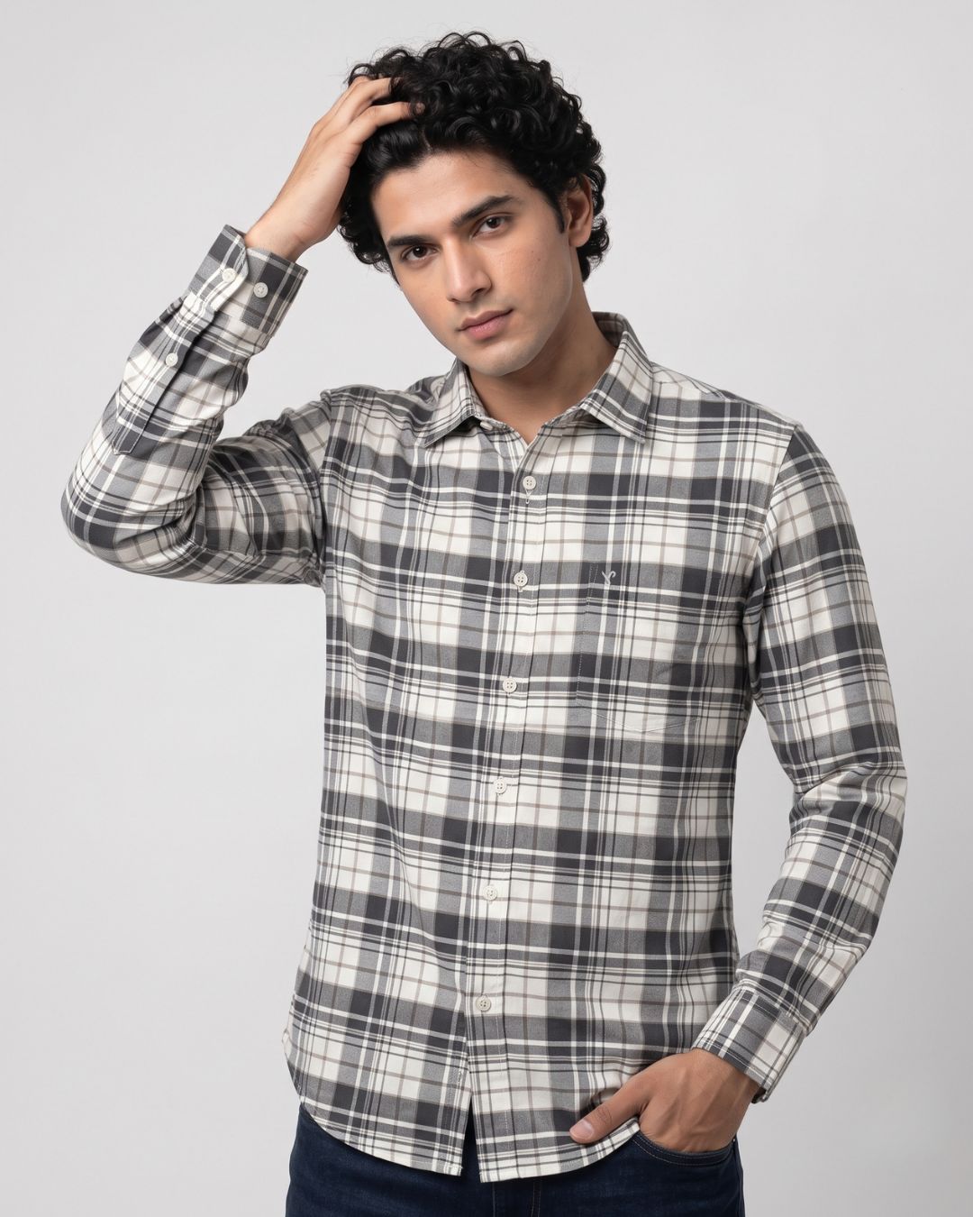 A man wearing a long-sleeve plaid button-up shirt in black, white, and gray, posed against a light gray studio background.